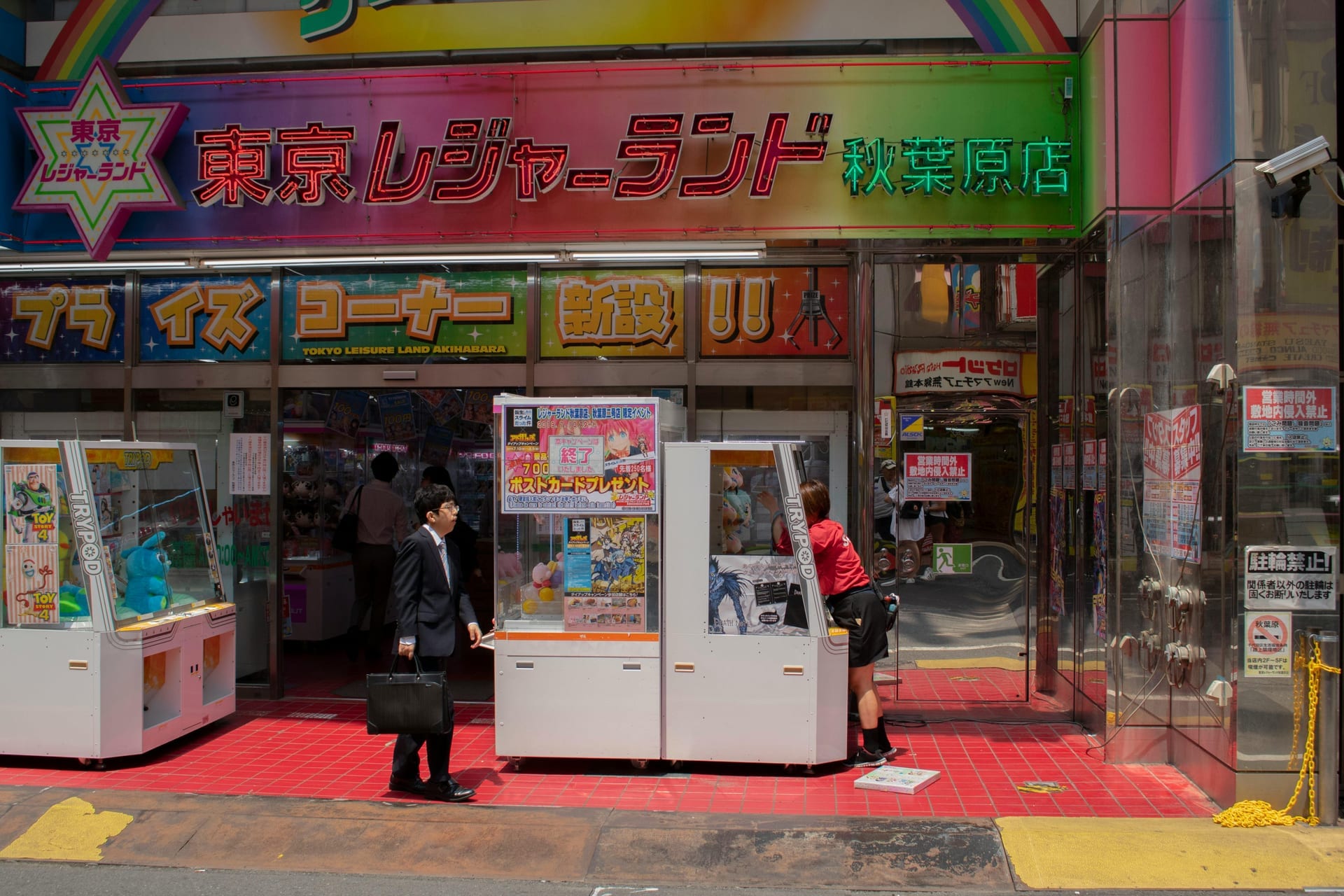 Multi-story Akihabara shopping building entrance covered in colorful anime posters, figure displays, and gaming store signage